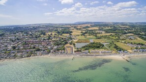 An aerial view of a coastal town with residential areas, a beach, and a large open field. - Seaview Holidays - Salterns Village (Seaview)