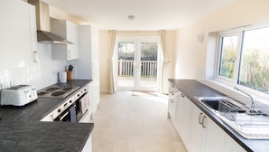A modern kitchen with a gas stove, a built-in oven, a sink, and a window overlooking a balcony. - Seaview Holidays - Salterns Village (Seaview)