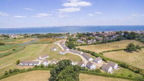 An aerial view of a coastal village with houses, a river, and a sea view. - Seaview Holidays - Salterns Village (Seaview)