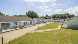 A row of single-story cottages with outdoor seating areas, a gravel path, and a grassy lawn. - Seaview Holidays - Salterns Village (Seaview)