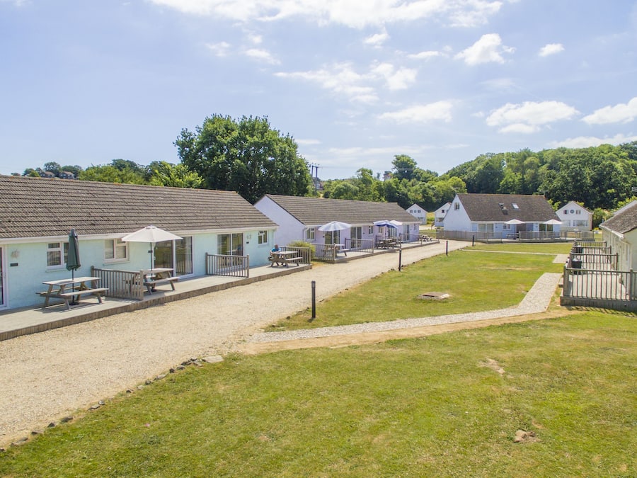 A row of single-story cottages with outdoor seating areas, a gravel path, and a grassy lawn.