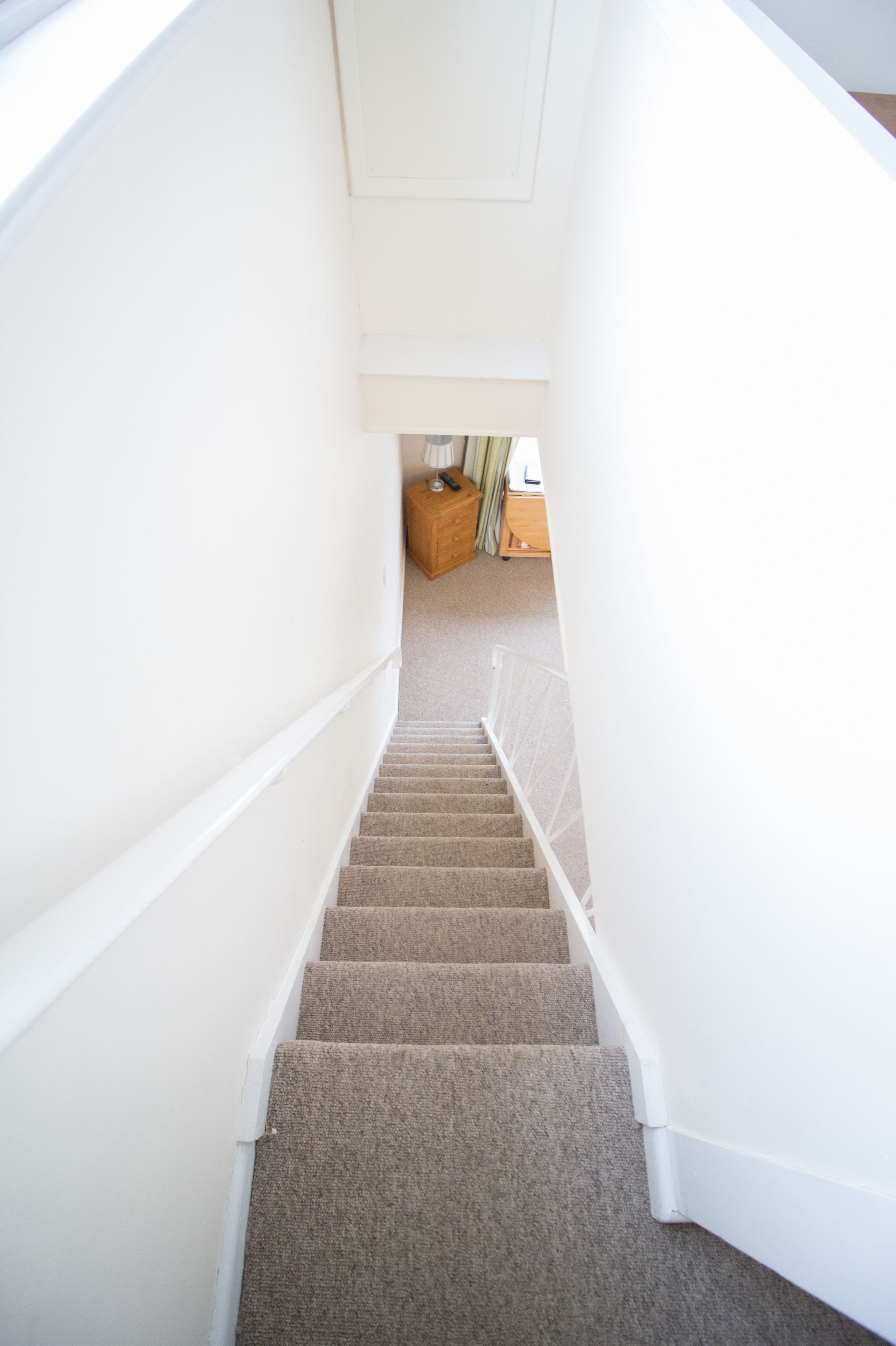 A carpeted staircase with white walls and a wooden bench at the bottom.