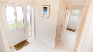 A hallway with white walls, a framed picture, and a door leading to a balcony. - Seaview Holidays - Salterns Village (Seaview)