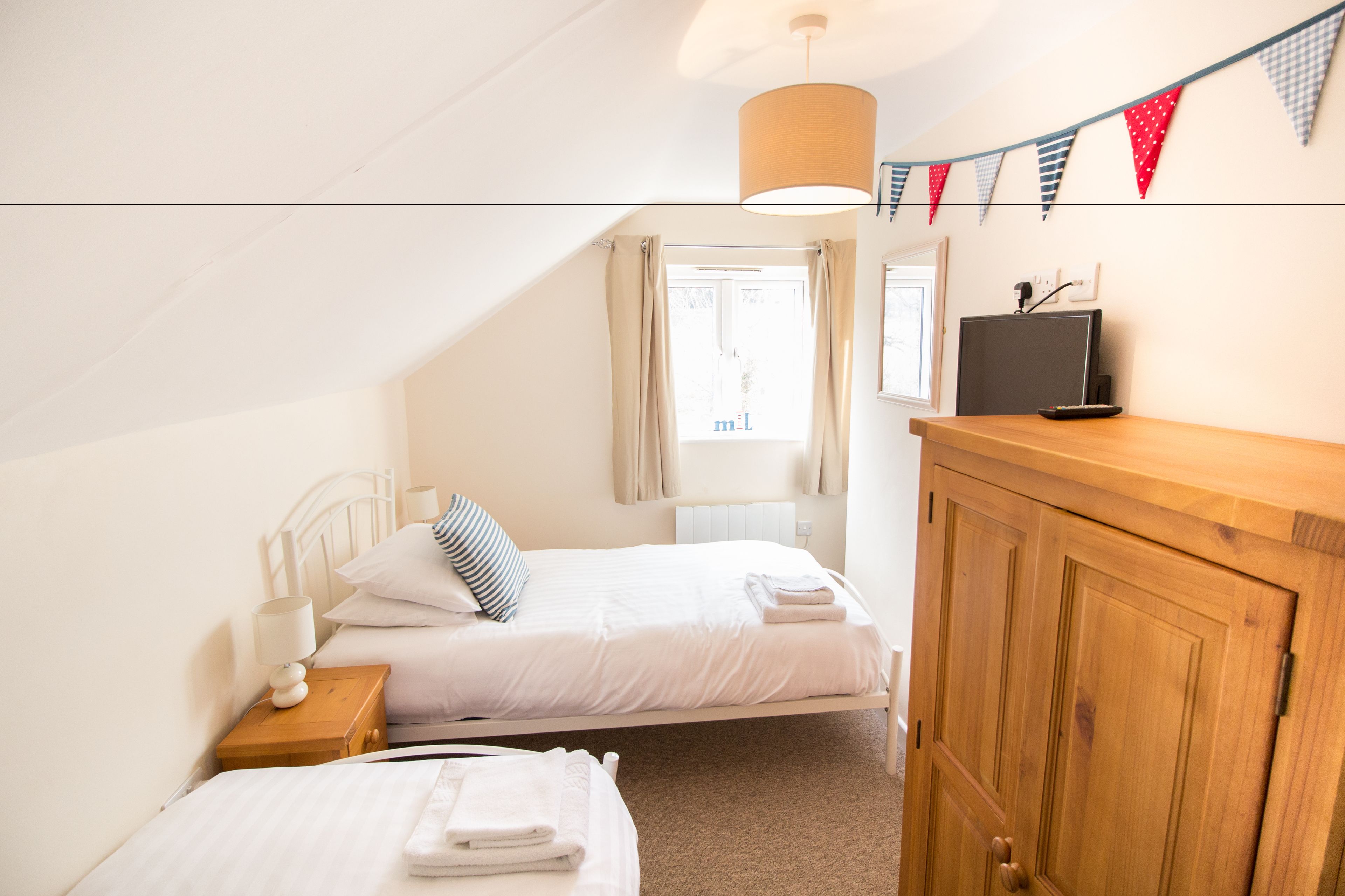 A bedroom with two beds, a wooden wardrobe, a desk, and a television.