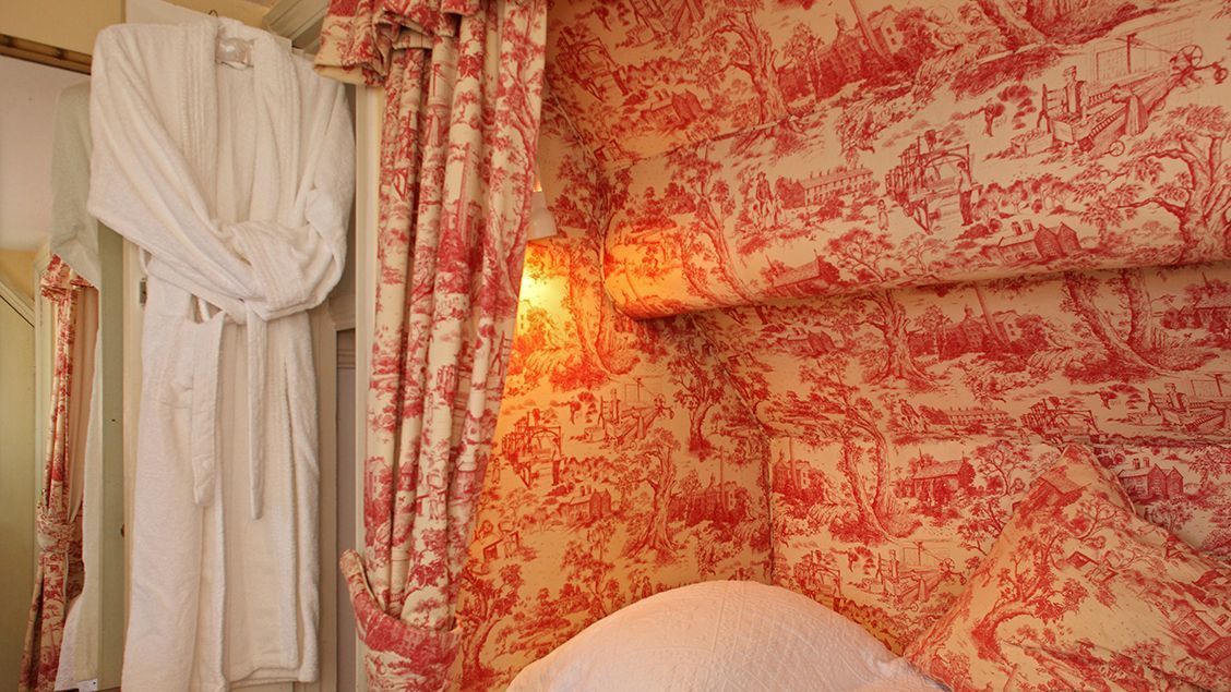 A room with a patterned wall, a hanging bathrobe, and a wall-mounted light fixture.