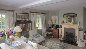 A cozy living room with a fireplace, a bookshelf, a comfortable sofa, and a dining area. - Cheltenham Cottage (Chipping Norton)