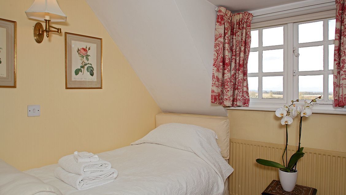 Un dormitorio con cama, ventana con cortinas florales, radiador y una orquídea en maceta.