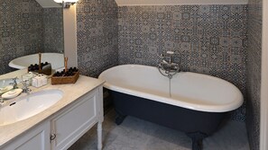 A bathroom with a freestanding bathtub, a sink, and a mirror. There are bottles and a basket on the counter. - Bookers Cottage (Chipping Norton)