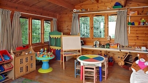 A cozy cabin with wooden walls, a play area with toys, a small table, and a window with curtains. - Sandown Cottage (Chipping Norton)