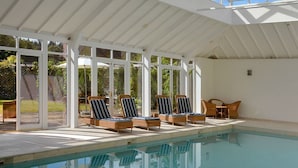 A covered pool area with lounge chairs and a table, surrounded by large windows. - Sandown Cottage (Chipping Norton)
