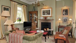 A traditional living room with a fireplace, comfortable seating, and a television. - Sandown Cottage (Chipping Norton)