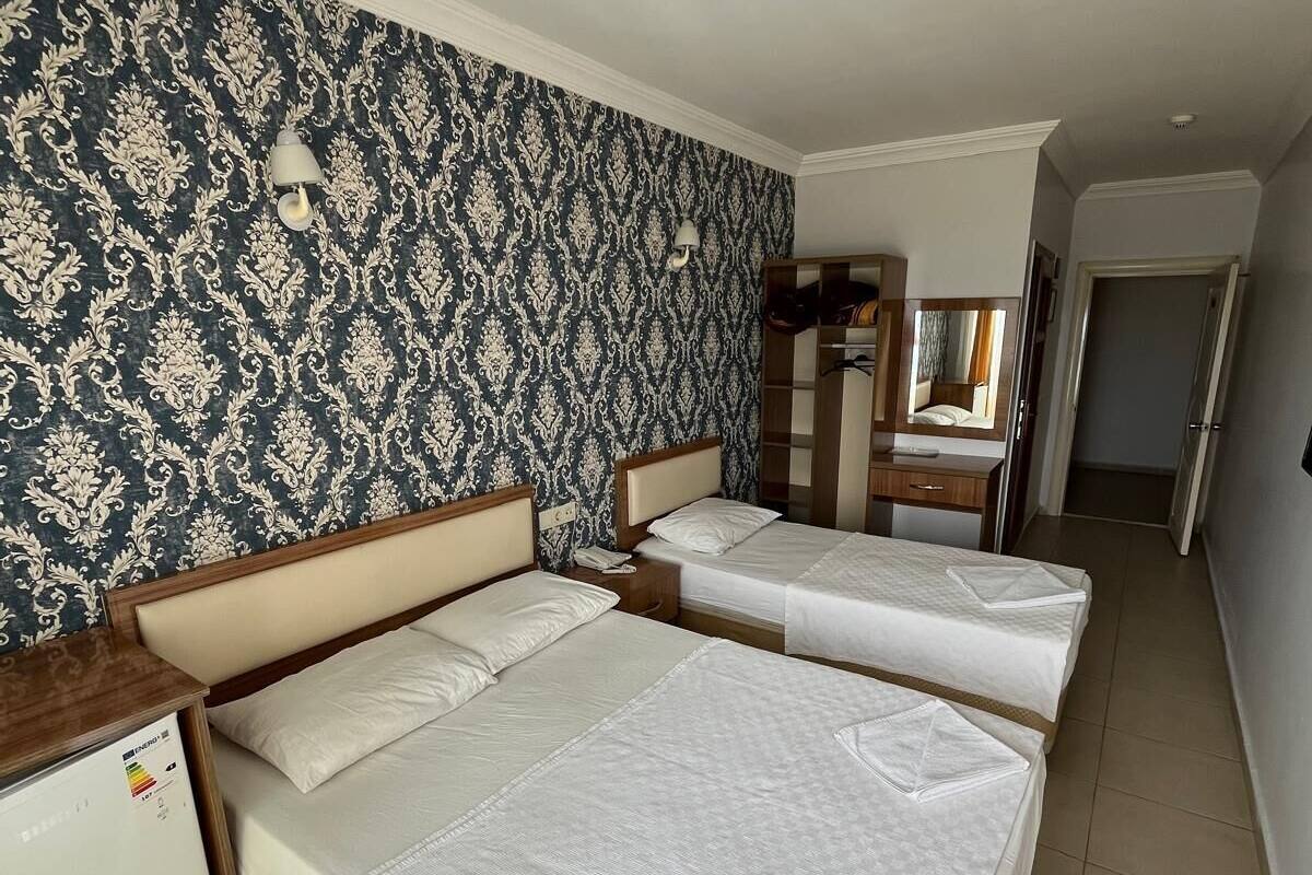 A hotel room with two beds, a small desk, a wardrobe, and a mirror.