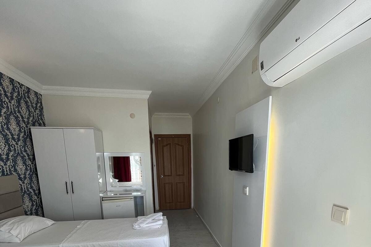 A hotel room with two beds, a wardrobe, a desk with a chair, a television mounted on the wall, and an air conditioning unit.