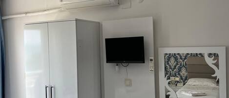 Una habitación con un armario blanco, un televisor de pantalla plana montado en la pared y un refrigerador pequeño.
