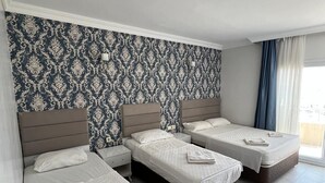 Habitación de hotel con tres camas, un papel tapiz estampado y un ventanal con cortinas.