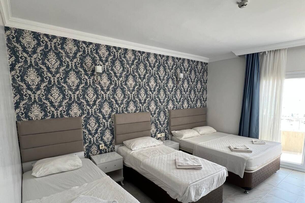 A hotel room with three beds, a patterned wallpaper, and a large window with curtains.