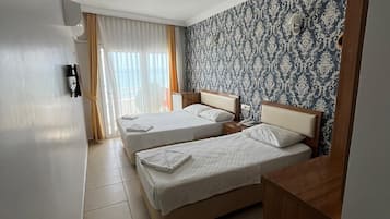 A hotel room with two beds, a wooden desk, a patterned wallpaper, and a window with curtains.