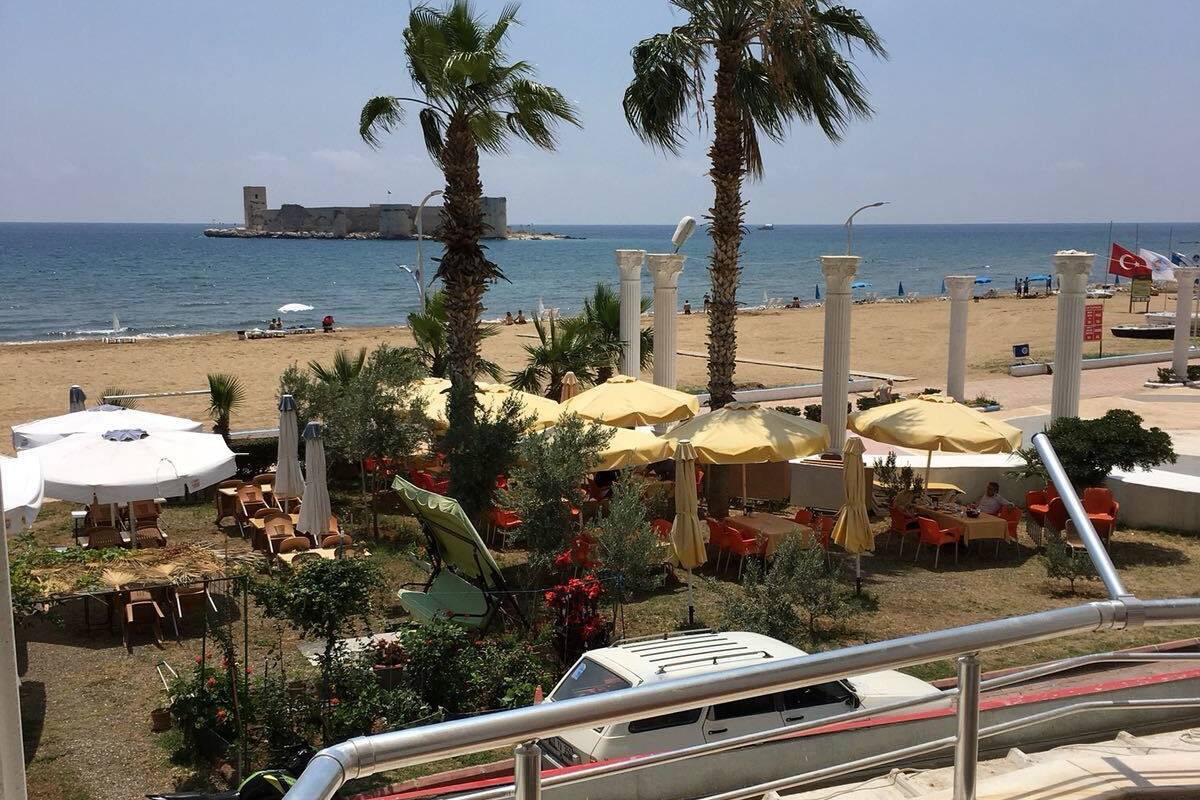 A beachside view with palm trees, umbrellas, and outdoor seating.