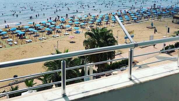 Una playa con numerosos sombrillas y tumbonas, cielo despejado y un barco a lo lejos.