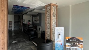 Zona de recepción de hotel con una lámpara de araña moderna, un mostrador de recepción y el letrero del hotel.