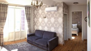 A living room with a sofa, patterned wallpaper, a chandelier, and a door leading to a bedroom. - Villa L'Orante (Lourdes)
