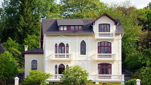 A large, two-story building with a symmetrical facade, multiple windows, and a balcony on the upper floor. - Villa L'Orante (Lourdes)