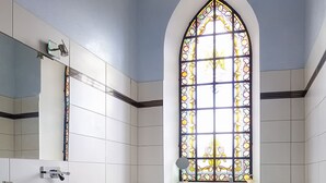 A bathroom with a large arched window, white tiled walls, a wooden vanity, and a mirror. - Villa L'Orante (Lourdes)