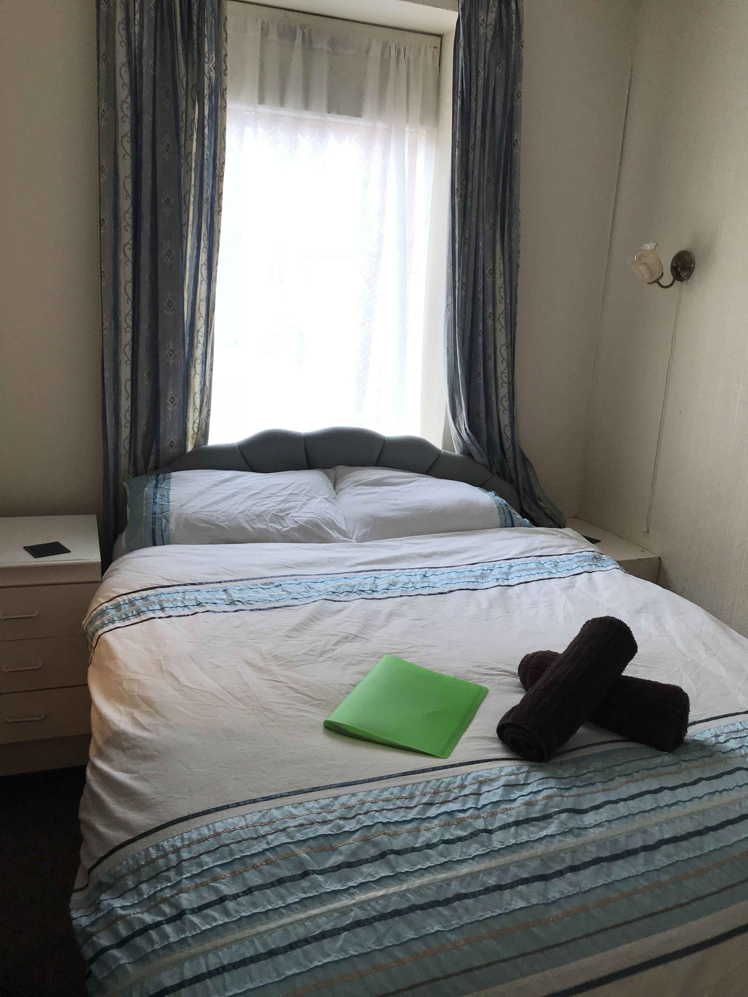 A neatly made bed with a striped bedspread, a green folder, and two rolled-up towels on the bed.