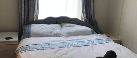 A neatly made bed with a striped bedspread, a green folder, and two rolled-up towels on the bed.