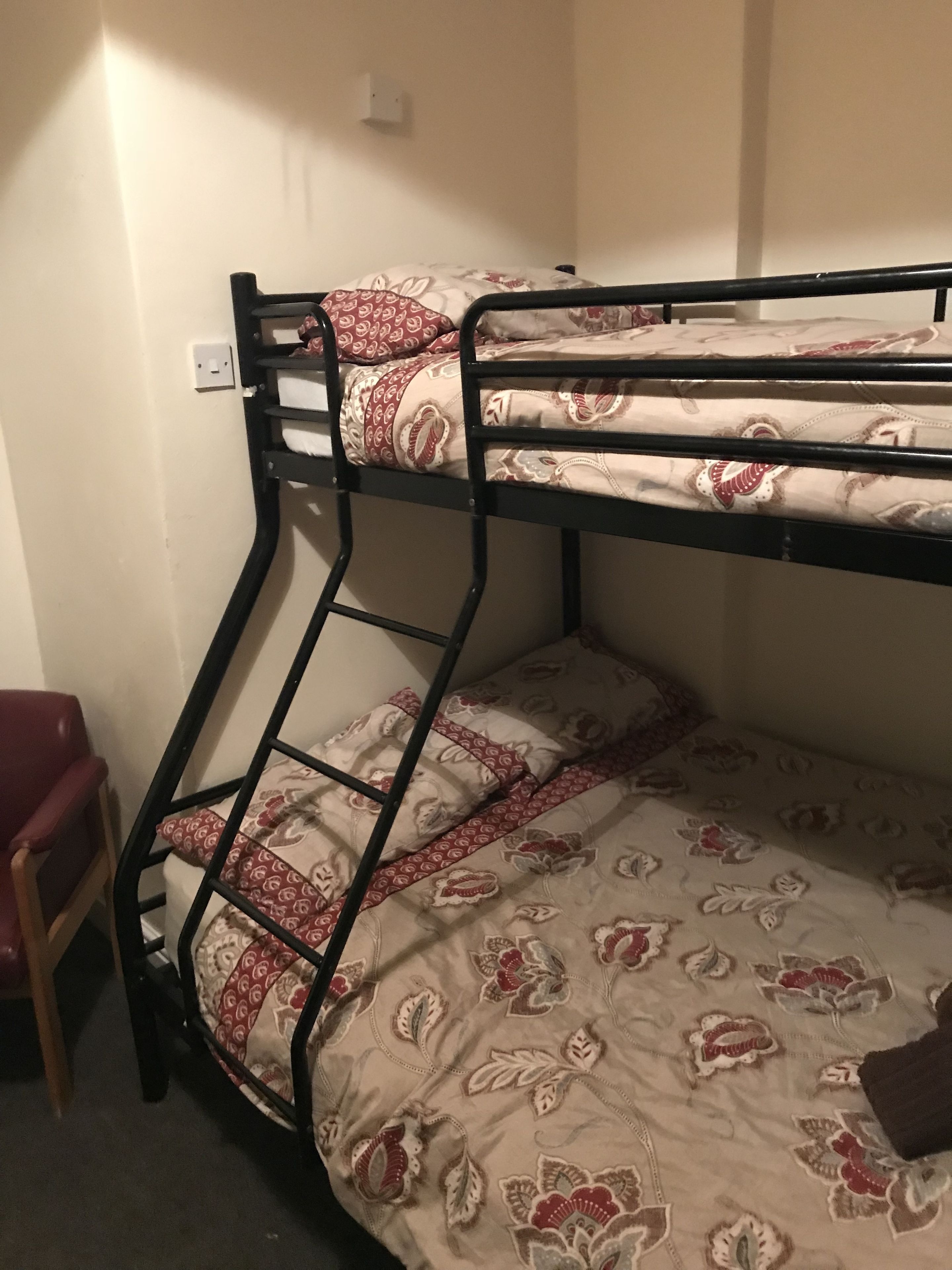 A bunk bed with patterned bedding, a wooden chair, and a wall socket.
