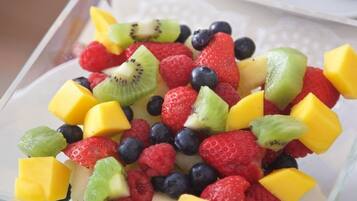 Un tazón de vidrio transparente lleno de frutas frescas variadas, como fresas, arándanos, frambuesas, kiwi y trozos de mango.