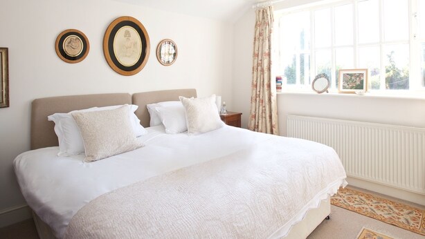 A neatly arranged bedroom with a large bed, a bedside table, and a window with curtains. - Hedingham Old Pottery (Halstead)