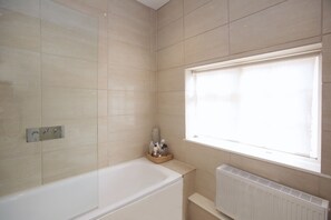 A bathroom with a bathtub, a window, and a radiator. - Hedingham Old Pottery (Halstead)