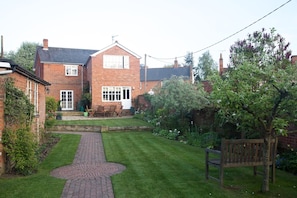 A brick house with a paved pathway leading to a wooden bench.
