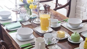 A breakfast table set with plates, bowls, a pitcher, and a jug, with chairs around it. - Hedingham Old Pottery (Halstead)