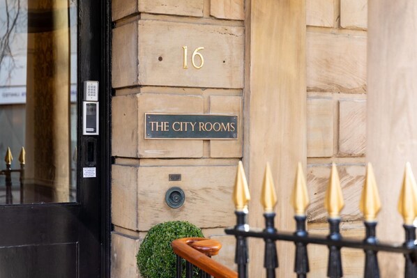 A building facade with a sign reading "16 THE CITY ROOMS" and a small green bush. - The City Rooms (Leicester)