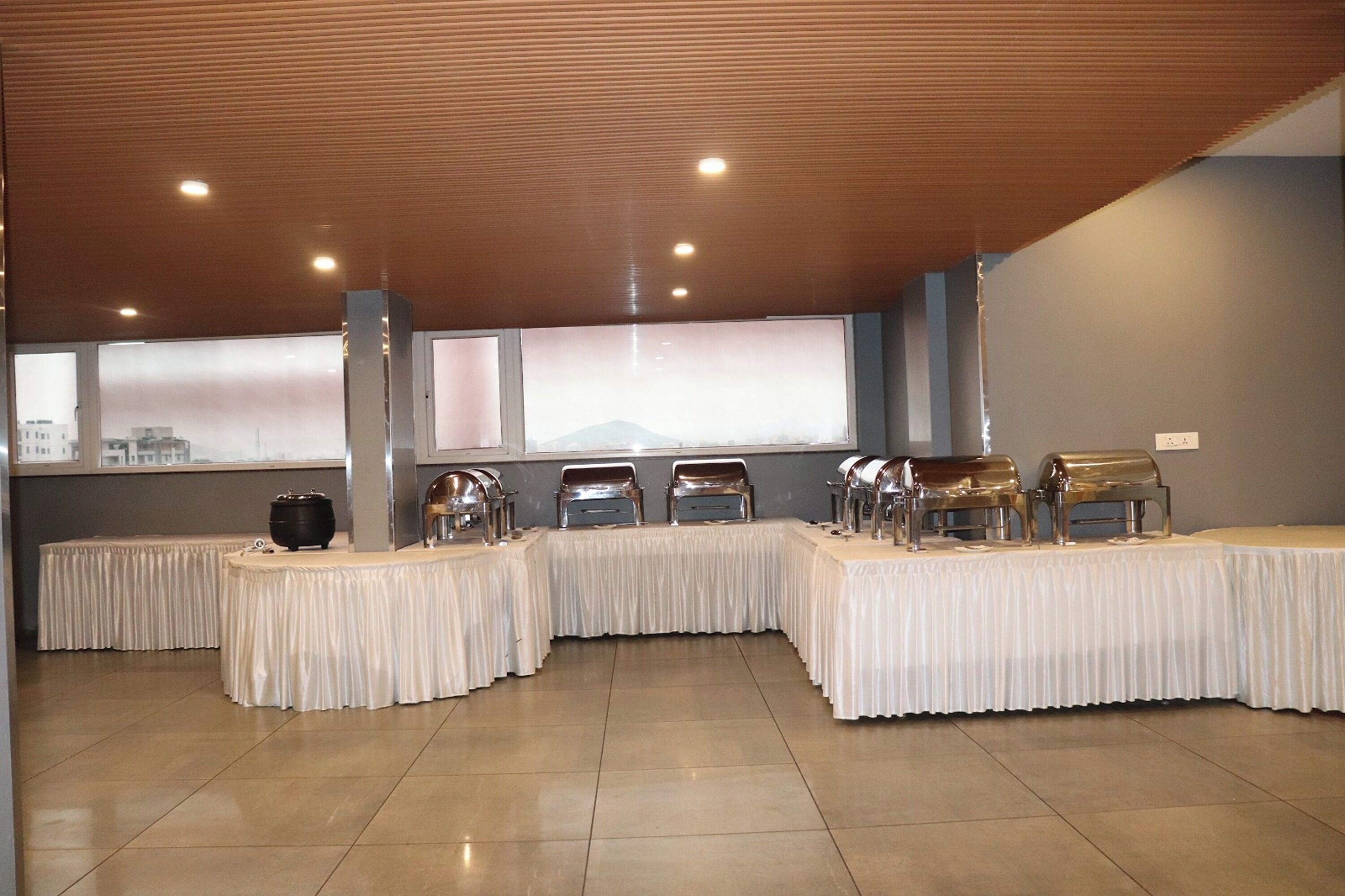 A buffet setup with multiple serving stations and a large window with a city view.