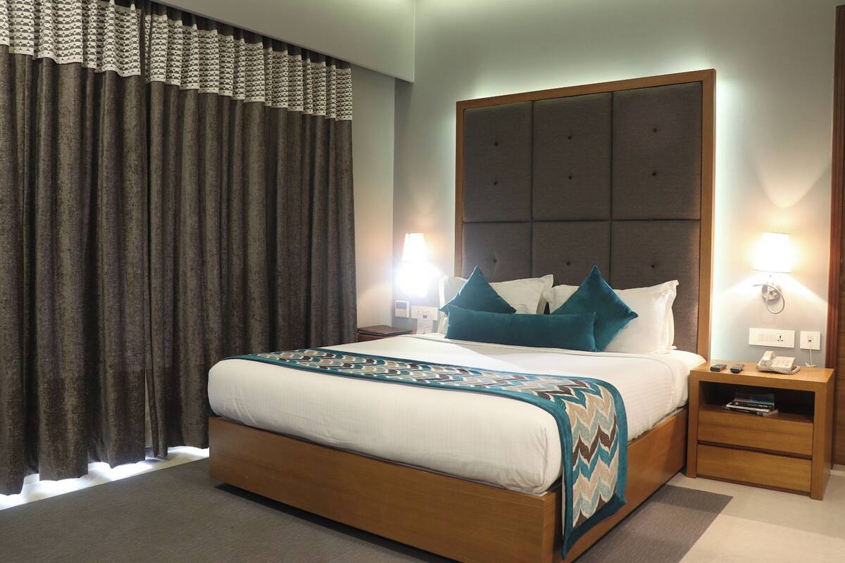 Una habitación de hotel con una cama grande, dos mesitas de noche y un ventanal con cortinas.