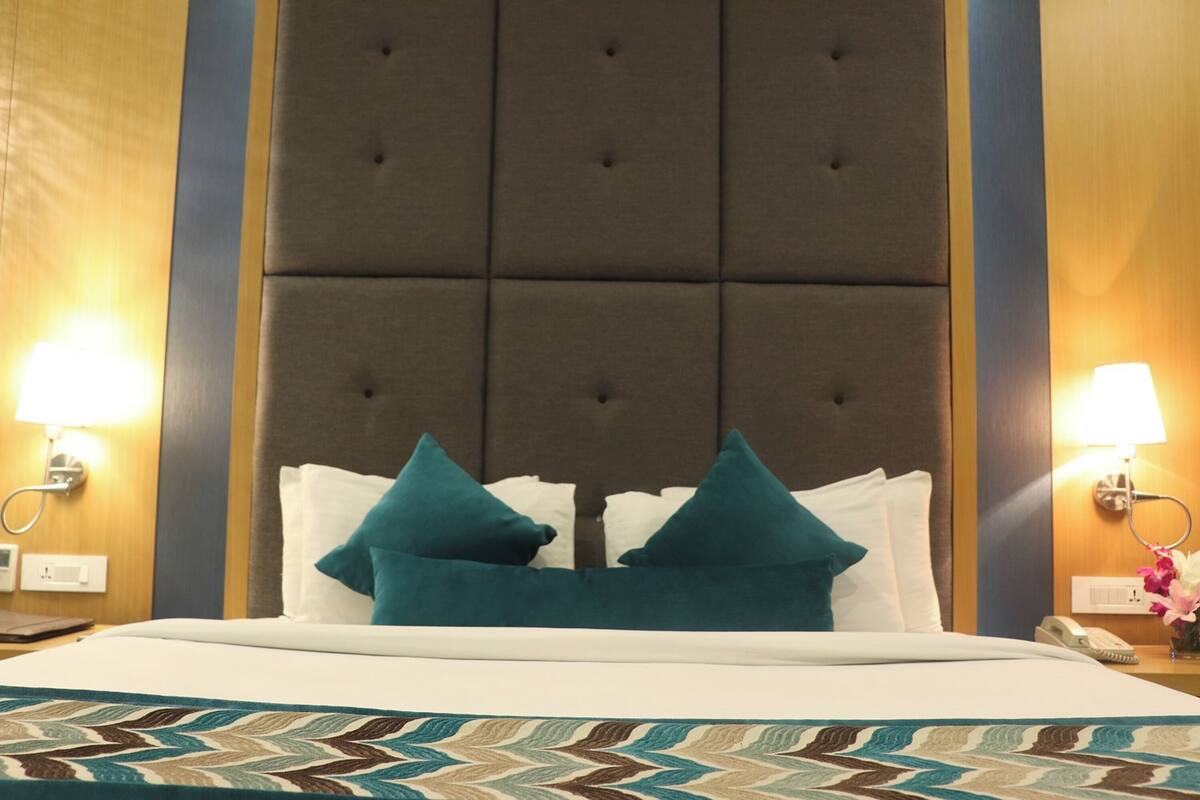 Habitación de hotel con una cama grande, dos almohadas, una colcha estampada, un cabecero capitonado y lámparas de noche.