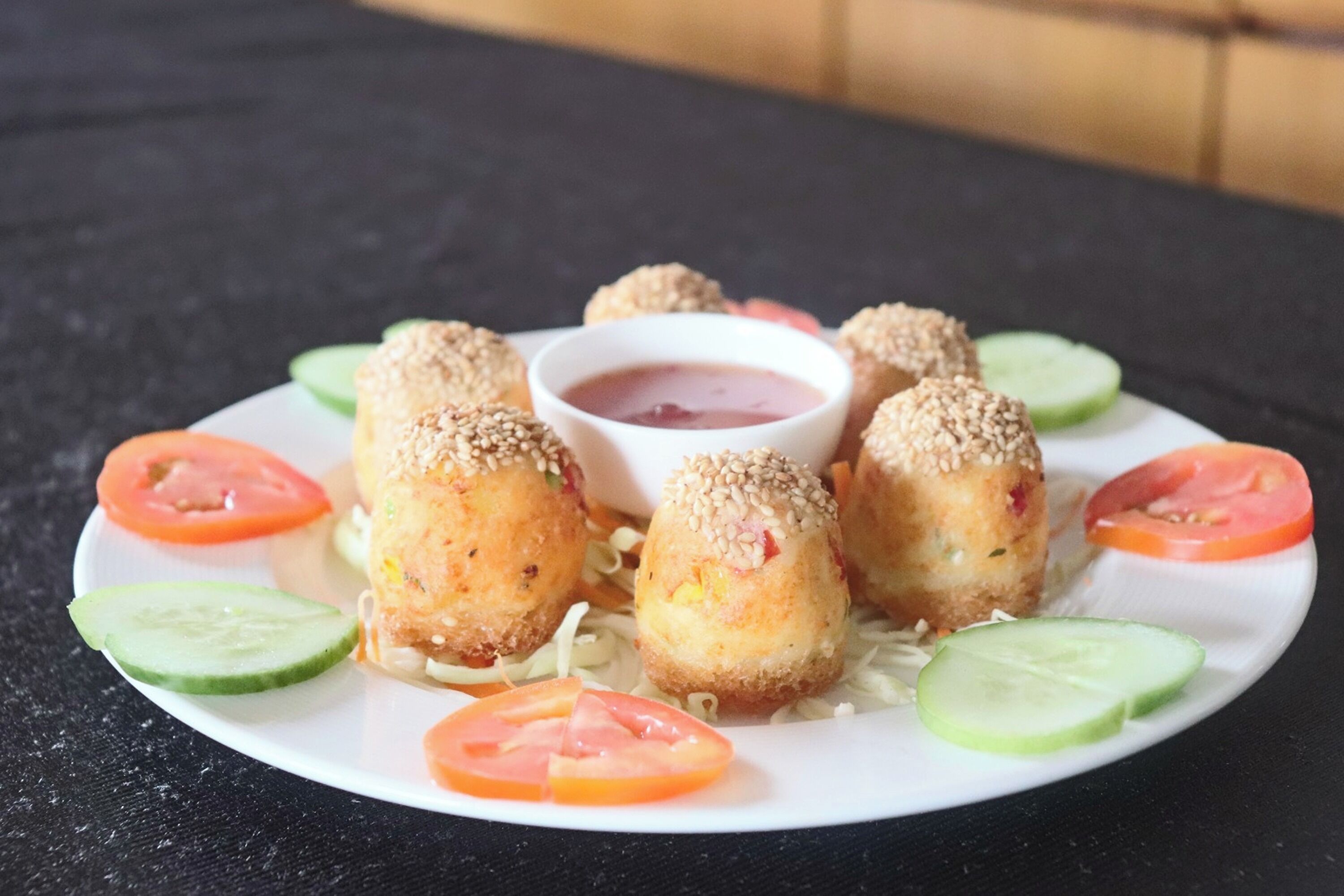 Ein Teller mit paniertem und frittiertem Gericht, dazu eine Dipsoße, Gurkenscheiben und Tomatenstücke.