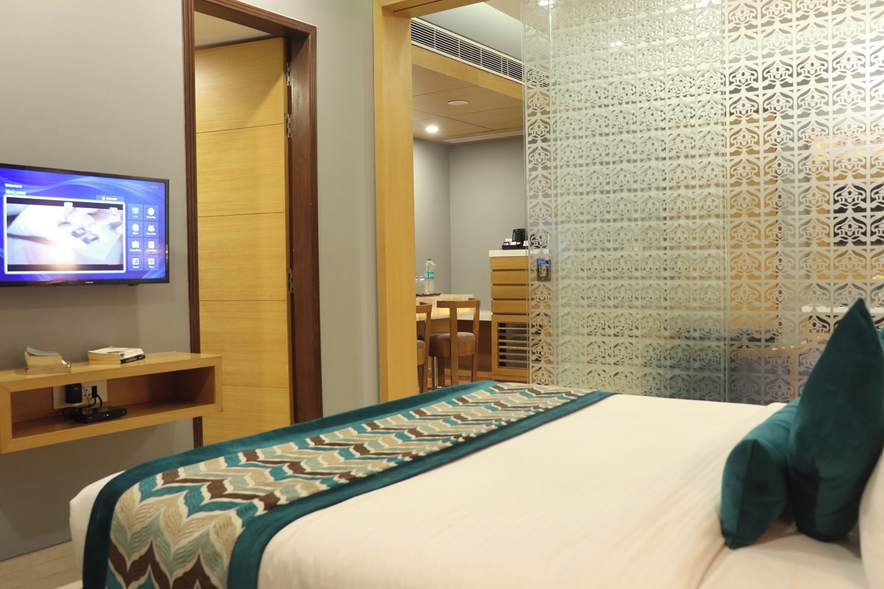 A hotel room with a bed, a TV on the wall, a wooden desk, and a patterned curtain.