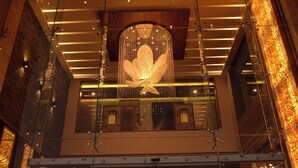 Un interior moderno con una gran lámpara floral iluminada colgando del techo, rodeada por barandas de vidrio y paneles de madera.