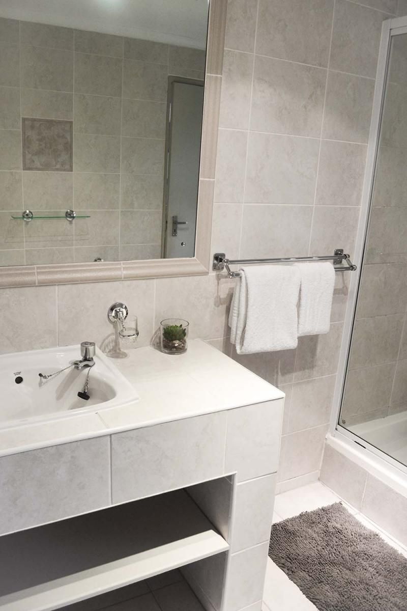 A modern bathroom with a glass shower enclosure, a white sink with a glass container, and a towel rack.