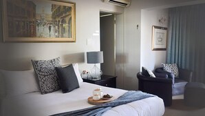 Habitación de hotel con una cama grande, una mesita de noche con lámpara, una silla y un cuadro en la pared.
