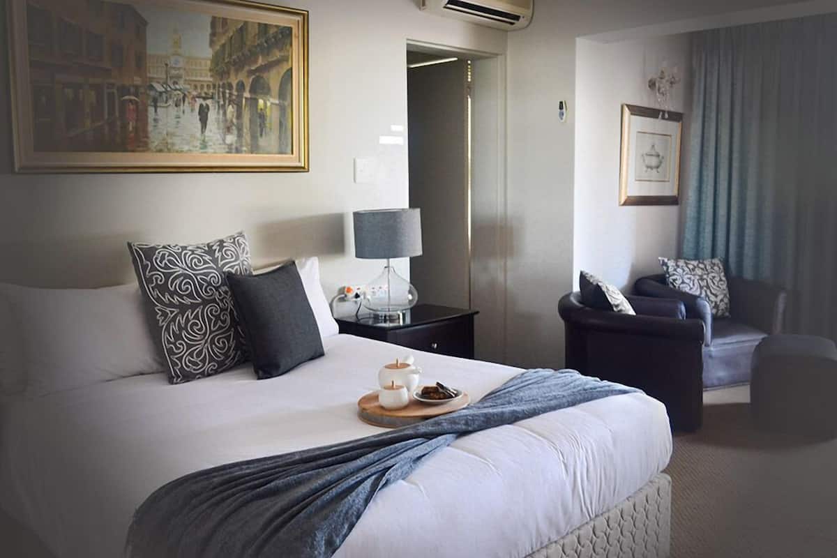A hotel room with a large bed, a nightstand with a lamp, a chair, and a painting on the wall.