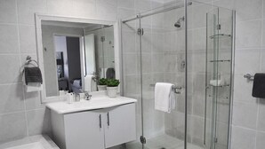 Un baño moderno con ducha de vidrio, tocador blanco con espejo y bañera.