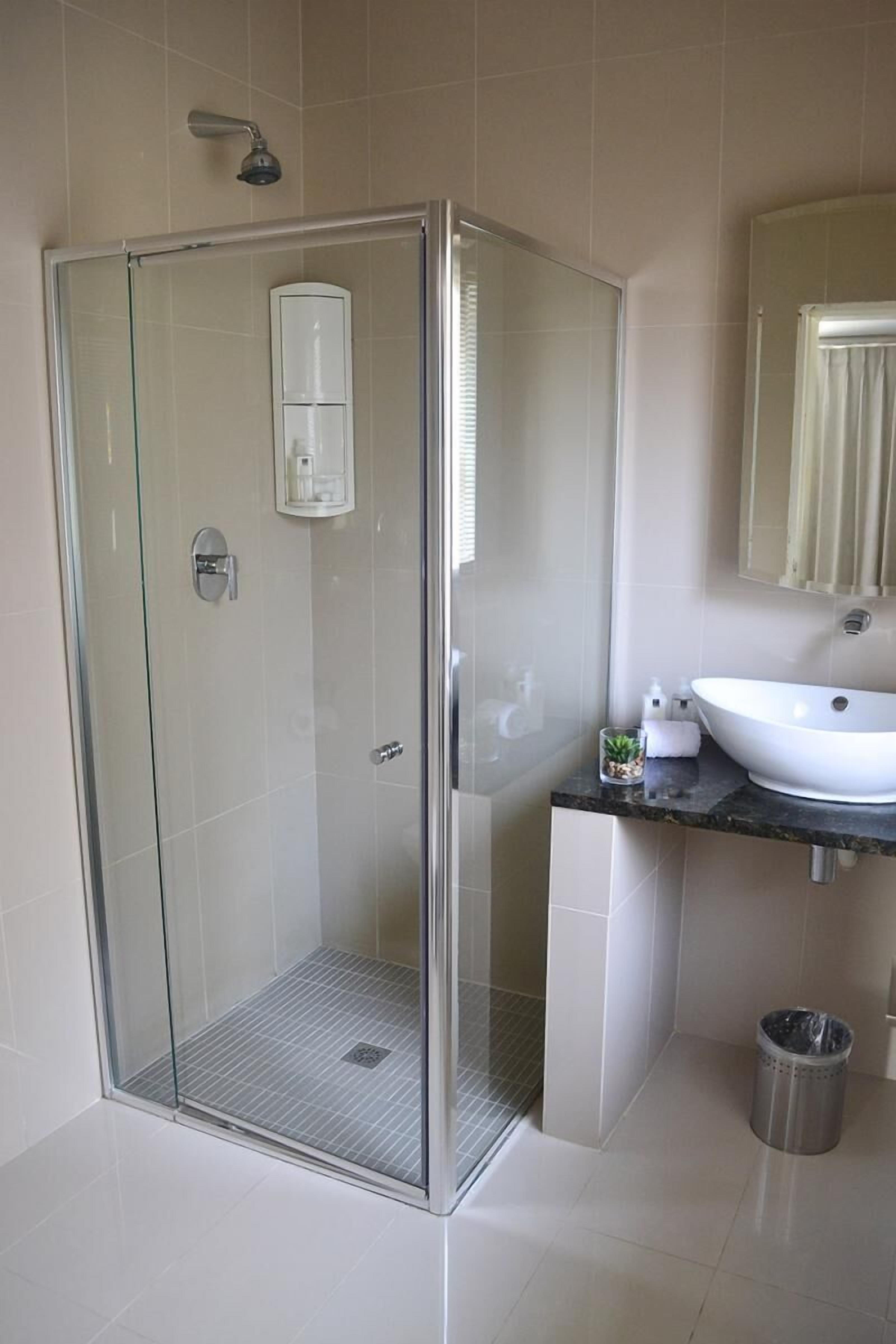 A modern bathroom with a glass-enclosed shower, a white sink, and a small trash bin.