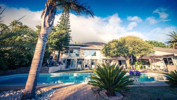 Una casa moderna con piscina, rodeada de palmeras y una montaña al fondo.