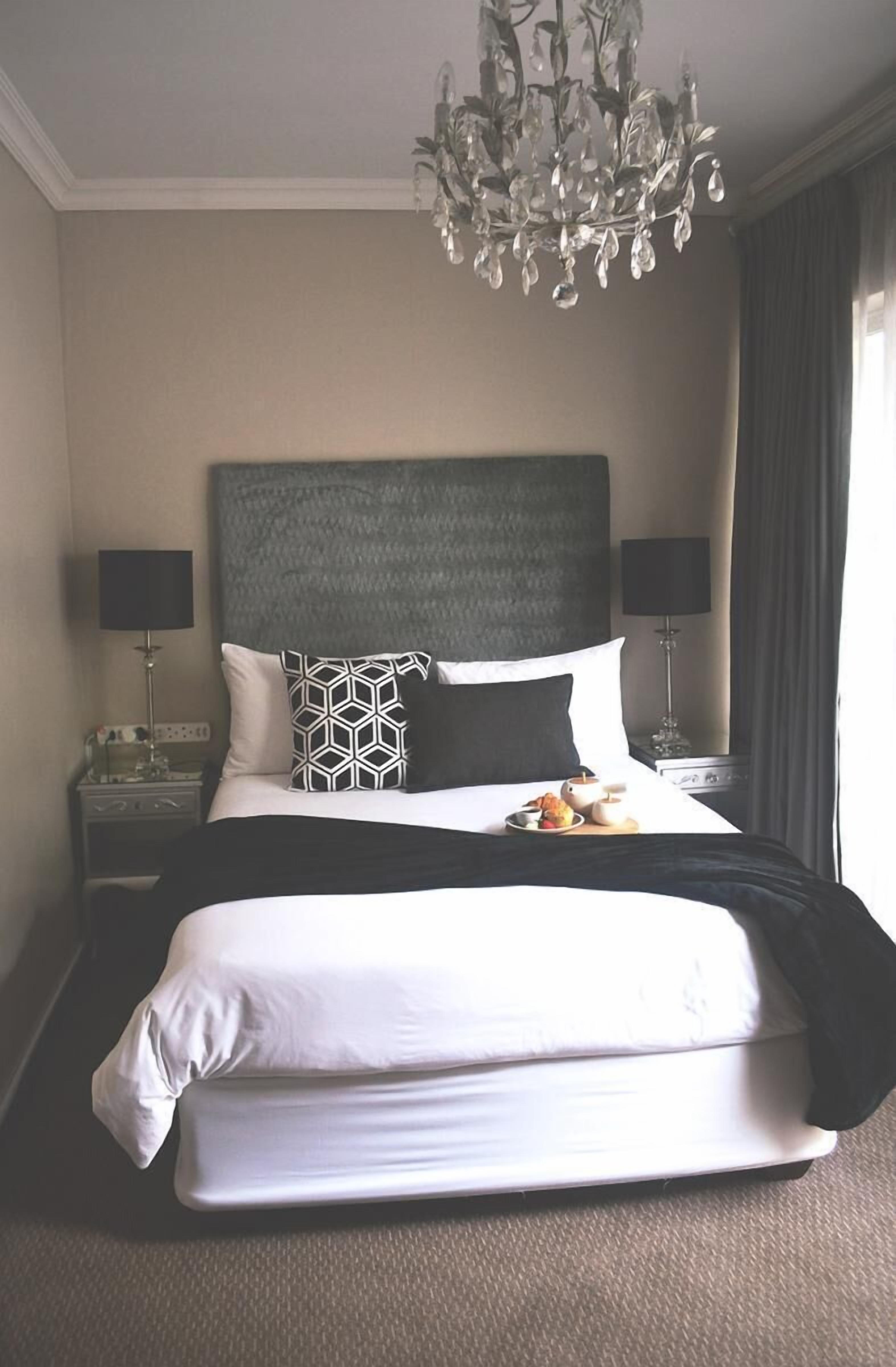 Een net opgemaakt bed met een gestreept kussen, twee bedlampjes, een kroonluchter en een nachtkastje met een lamp.