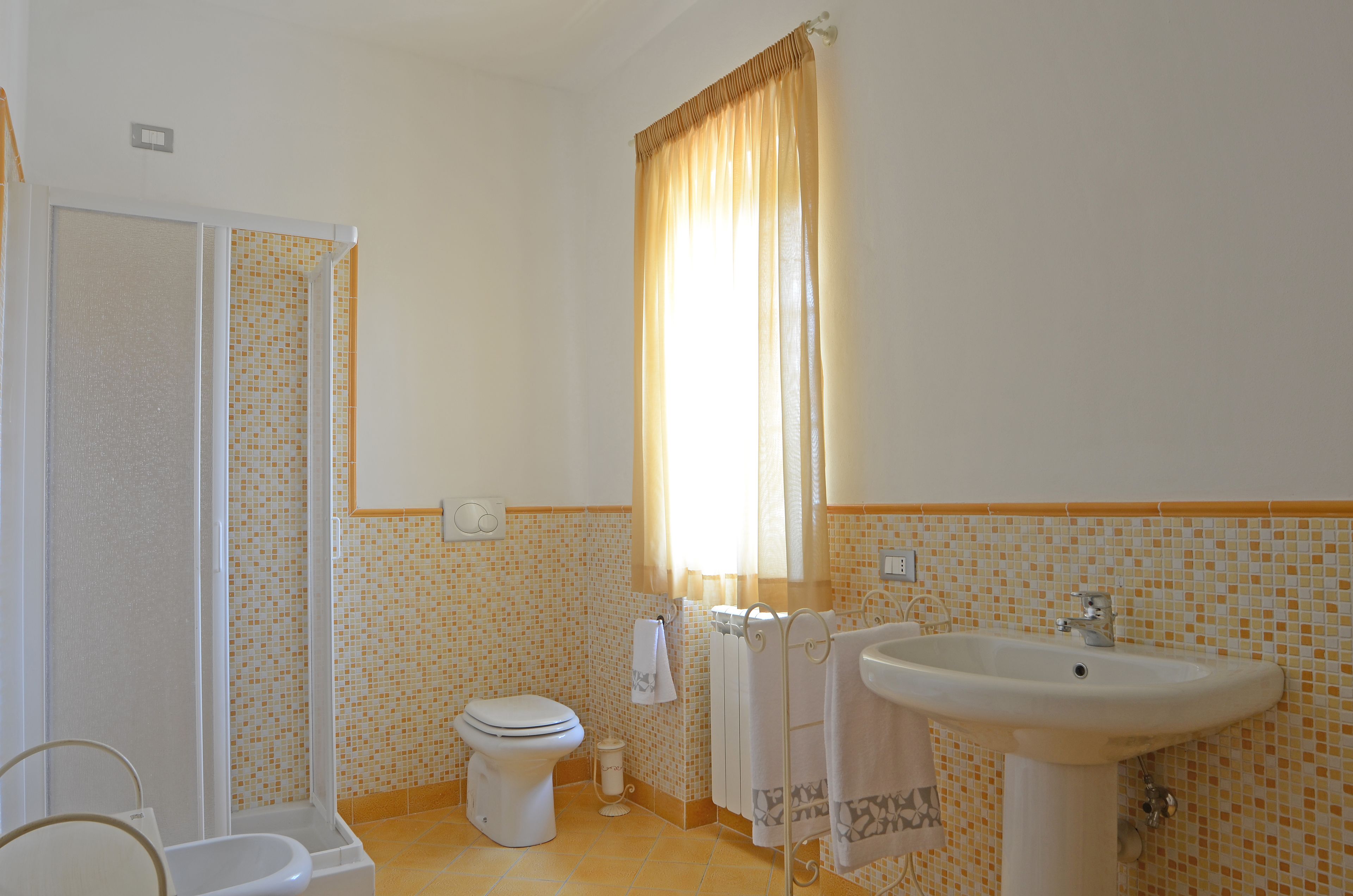 A bathroom with a shower, toilet, sink, and a window with curtains.